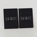 Pack of two small mini notebooks showing the phases of the moon against a starry space background.