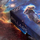 Pillars of Creation puzzle - 1000 piece rectangular space puzzle.of the Eagle Nebula - showing corner of box with puzzle pieces in the background